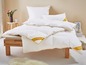 Een wit dekbed van Palette met een beige rand op een houten bed.