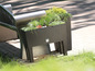 Een bruine plantenbak met verschillende planten op een terras.