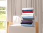 Een stapel beddengoed in verschillende kleuren op een witte fauteuil.