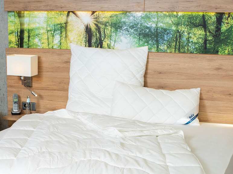 Une couette blanche avec un oreiller Beco sur un lit avec une tête de lit en bois.