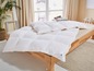 Une couette en duvet blanche Malou et une couette sur un lit en bois.