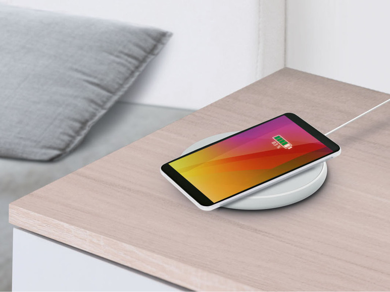 Un smartphone sur un chargeur sans fil sur une table en bois.