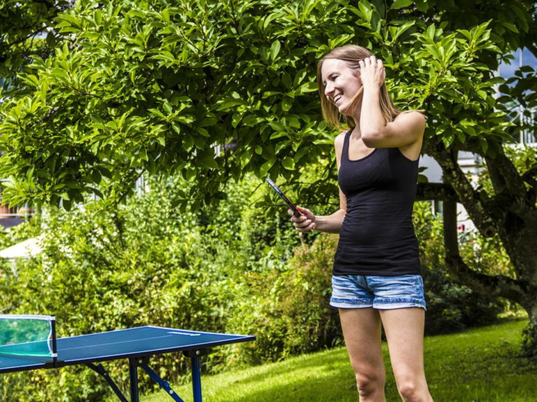 Een vrouw met een pingpongbat staat bij een tafeltennistafel buiten.
