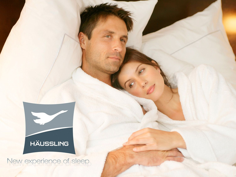 Un couple en peignoirs blancs, allongé dans un lit, avec le logo Häussling.