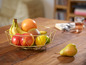 Een gouden fruitmand met bananen, appels, een grapefruit, mango en een peer.