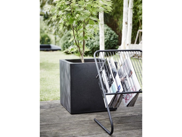 Een zwarte plantenbak met een tijdschriftenrek ernaast.