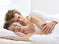 Een stel slaapt in bed met kussens en dekbedden.