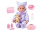 Une poupée dans une combinaison violette avec un ours en peluche, une sucette, un biberon, une assiette, des couverts et des produits de soins.