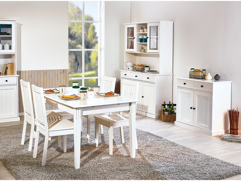 Witte eettafel met stoelen, dressoir en vitrinekast in een eetkamer.