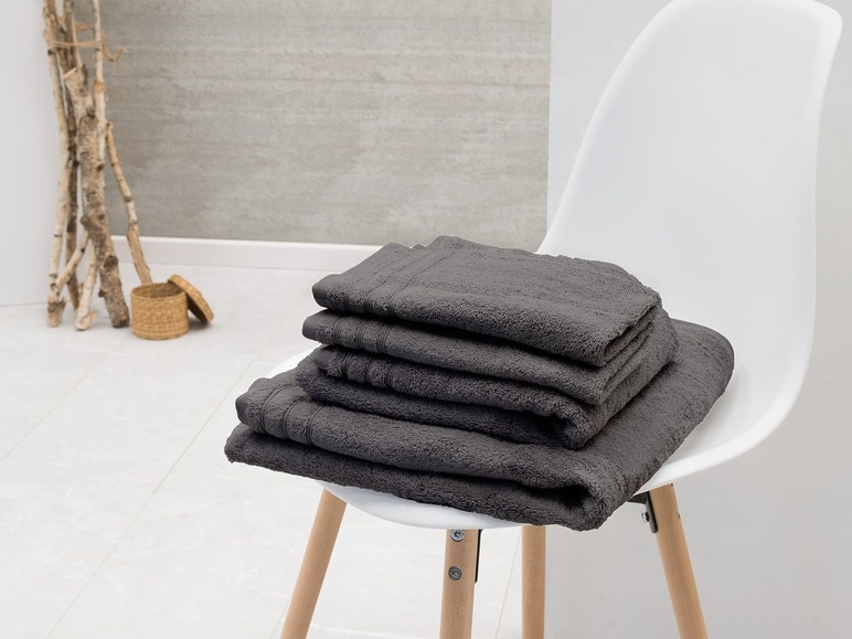 Une pile de serviettes de bain gris foncé sur une chaise blanche.