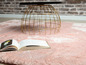 Un tapis en fourrure rose avec une table basse dorée et un livre ouvert.