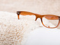 Des lunettes avec une monture marron sur un tapis blanc et moelleux.