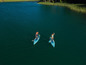 Twee personen peddelen op opblaasbare paddleboards op een meer.
