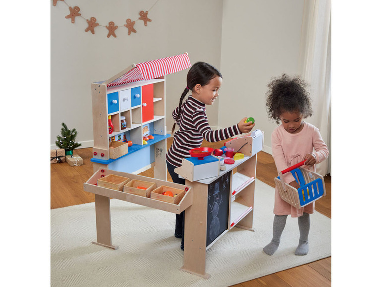 Deux enfants jouent à la boutique avec un stand en bois et un panier d'épicerie.