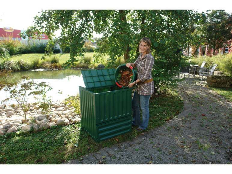 Een vrouw gooit bladeren in een groene compostbak.