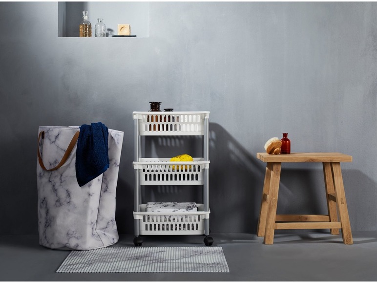 Une salle de bain avec un panier à linge, un chariot de rangement et un tabouret en bois.