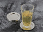 Un verre avec une boisson sur un dessous-de-verre argenté avec une pile de dessous-de-verre argentés à côté.
