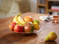 Een koperen fruitmand met bananen, appels, mango en citroenen.