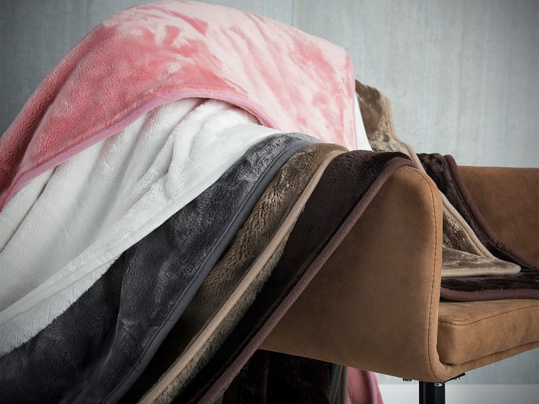 Plusieurs couvertures douces en rose, blanc, gris et marron sur une chaise.