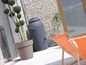 Een grijs regenton en een terracotta bloempot op een terras met twee ligstoelen.