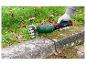 Taille-herbe portatif avec une personne coupant l'herbe le long d'une bordure en pierre.