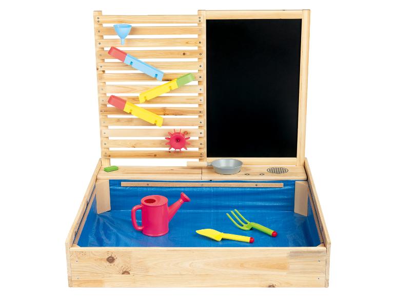 Een houten zandbak met een waterbaan, een krijtbord en tuingereedschap.
