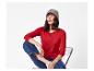 Vrouw in rode longsleeve, blauwe jeans en grijze muts zittend op een stoel.