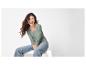 Lachende vrouw in een groen shirt met lange mouwen en jeans, zittend op een wit platform.