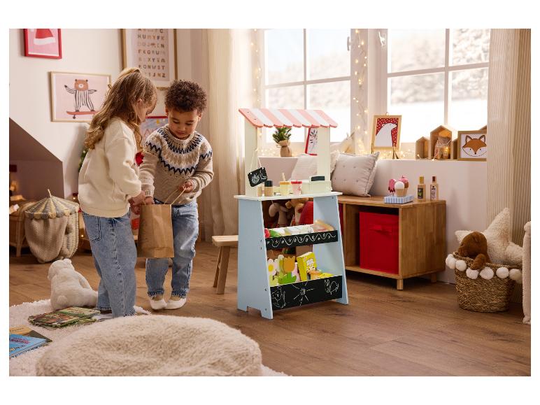 Deux enfants jouent avec un étal de marché en bois et des jouets dans une pièce décorée pour les fêtes.