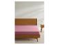 Drap-housse rose sur un lit avec cadre en bois et table de chevet.