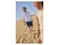Homme en chemise blanche et short bleu foncé marchant sur une dune de sable.