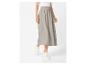 Vrouw draagt een lichtgrijze midirok met een witte top en witte sneakers.