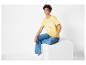 Een vrouw draagt ​​een gele T-shirt met de tekst 'Good Vibes Only' en blauwe jeans.