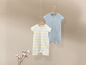 Twee babypakjes, een met strepen en een effen blauw, hangen aan hangers.