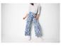Femme en pantalon large à motif cachemire bleu et blanc, haut blanc et baskets.
