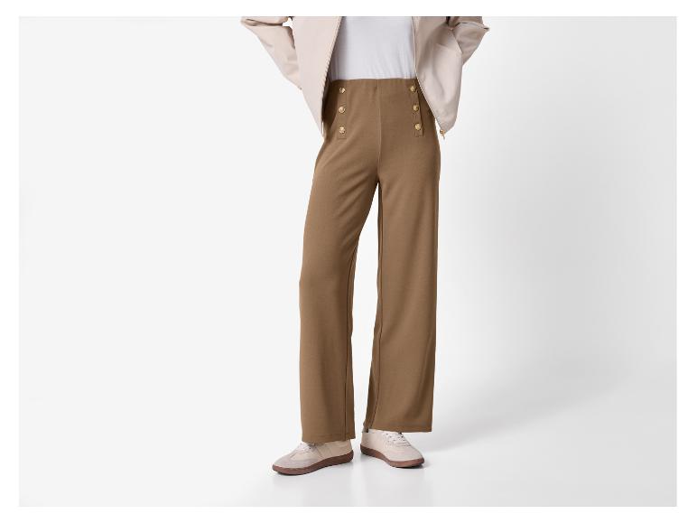 Bruine wijde broek met gouden knopen en beige sneakers.