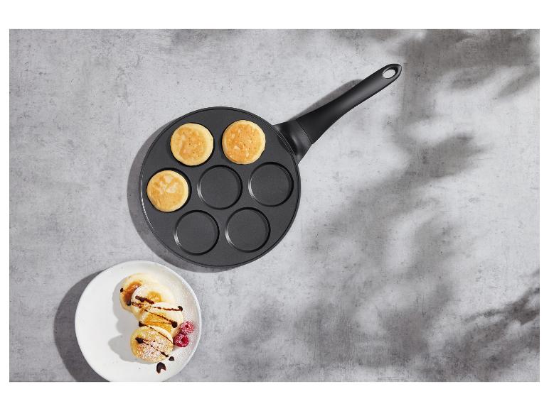 Poêle avec des crêpes et une assiette de crêpes décorées sur une surface en béton.