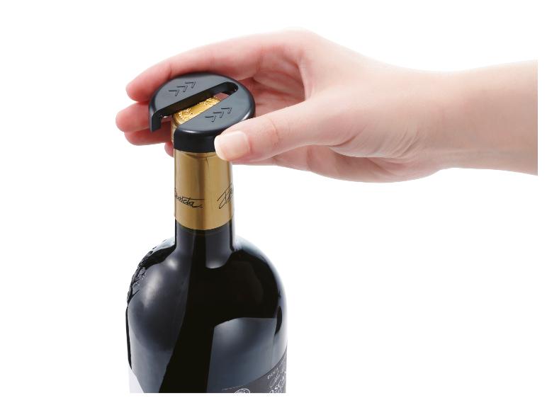 Een hand opent een fles rode wijn met een zwarte dopopener.