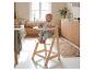 Bébé souriant dans une chaise haute en bois, mangeant des biscuits et des myrtilles dans une cuisine lumineuse.