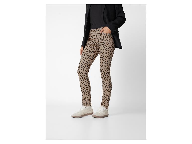Une personne portant un blazer noir, un haut noir, un pantalon imprimé léopard et des baskets beiges.