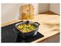 Vierkante pan met pasta en groenten op een inductiekookplaat, olie en peper op de achtergrond.