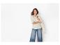 Femme en t-shirt rayé, jean large et veste claire drapée sur son bras.
