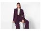 Vrouw in een donkerpaarse blazer en bijpassende broek, zittend op een witte doos.