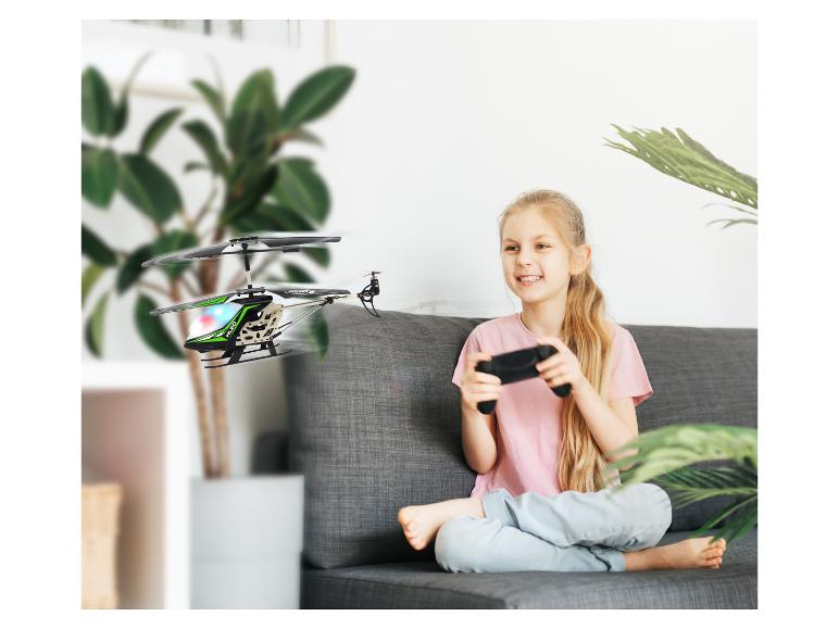 Fille souriante sur le canapé contrôlant un hélicoptère jouet télécommandé.