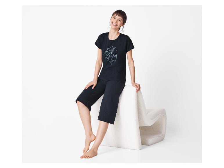 Une femme en pyjama noir à imprimé assise sur un pouf blanc.