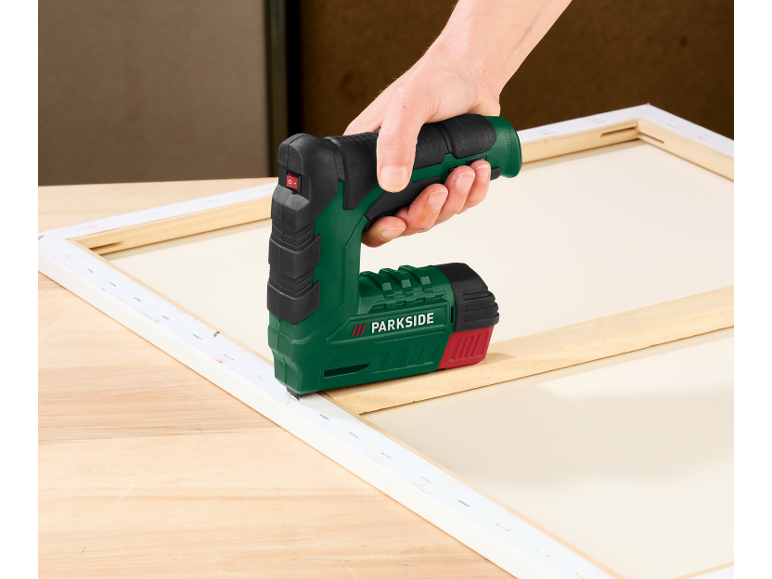 Een hand gebruikt een elektrische tacker om canvas aan een houten frame te bevestigen.