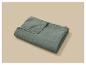 Couverture matelassée vert sauge pliée avec surpiqûres sur fond beige.