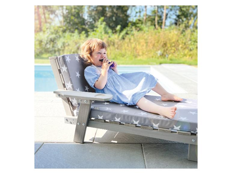 Jeune enfant en robe bleue se détendant sur une chaise longue à motifs d'étoiles près de la piscine.