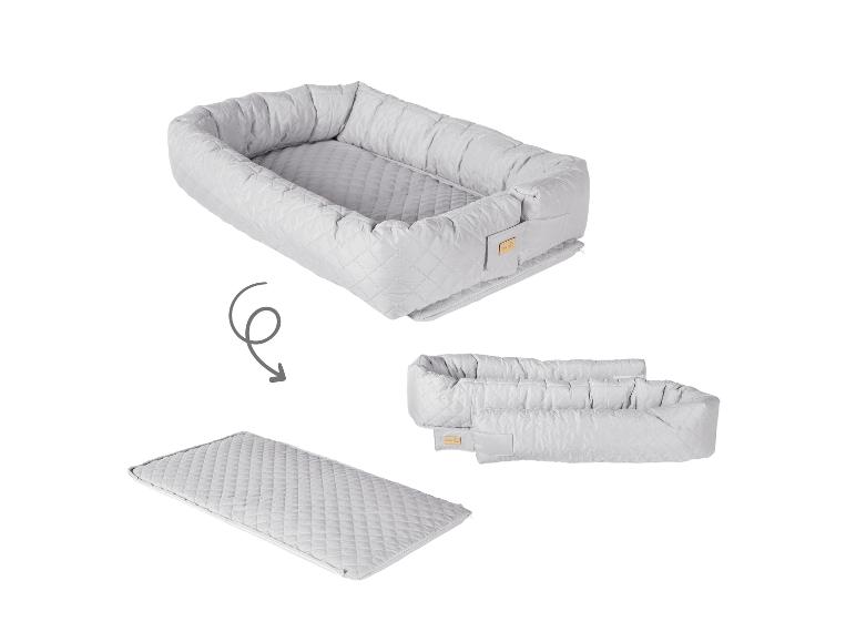 Grijze, gewatteerde babynest die uitklapt tot een matras, met een pijl die de transformatie toont.