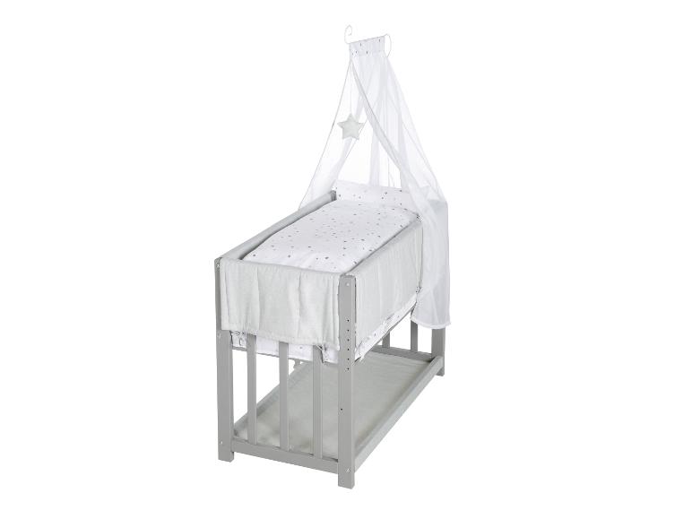 Grijze houten babywieg met een wit hemeltje en beddengoed met sterren.